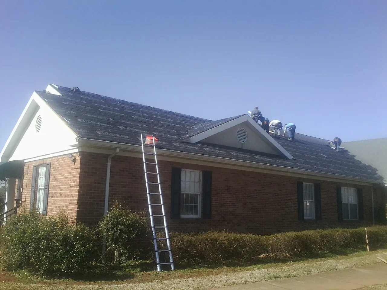 Crew tearing shingles off a brick ranch roof with a ladder set — Metal Roof Repair work by our crew in Granite Quarry
