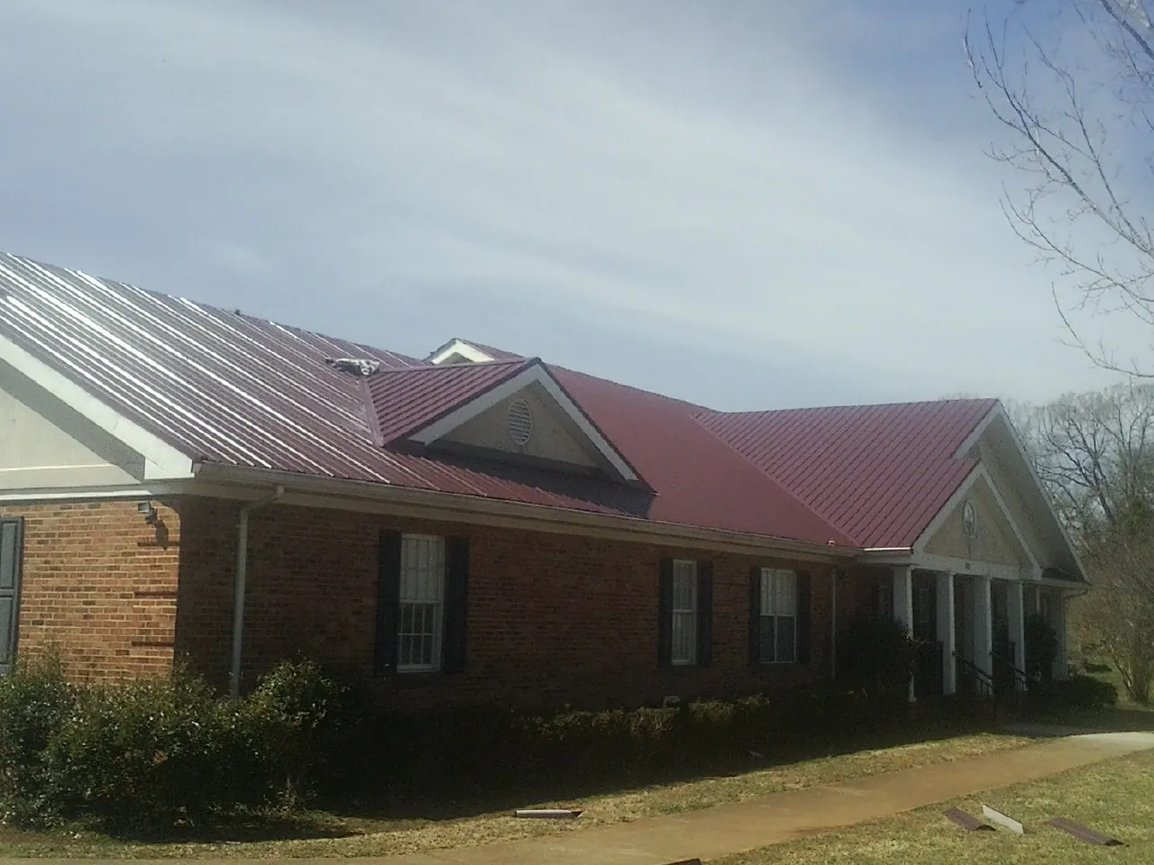Red metal roof with gabled entries on a long brick building, from a Hail Damage Roof Repair job in Granite Quarry