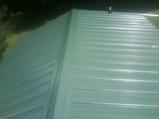 New green metal panels meeting at the ridge of a roof — Flat Roof Repair work by our crew in Granite Quarry