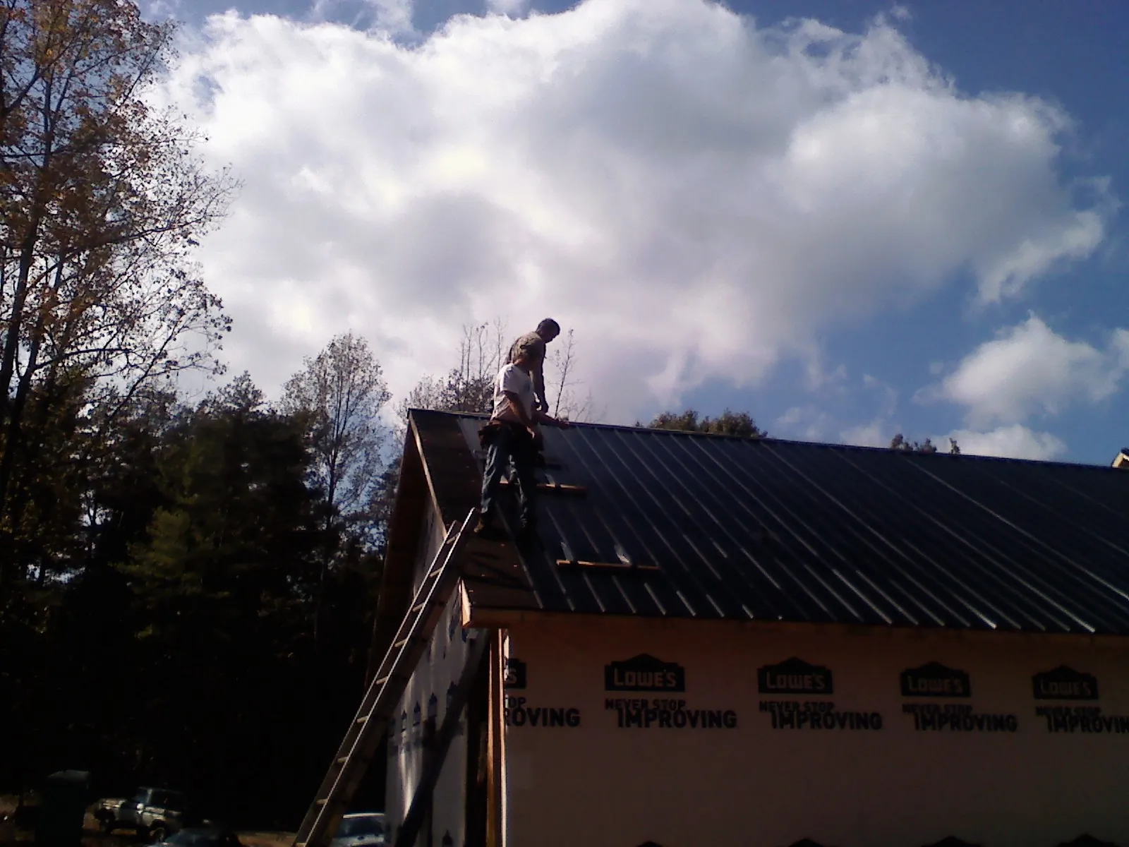 Roofer fastening dark metal panels high against a cloudy sky, from a Roof Inspection job in Granite Quarry
