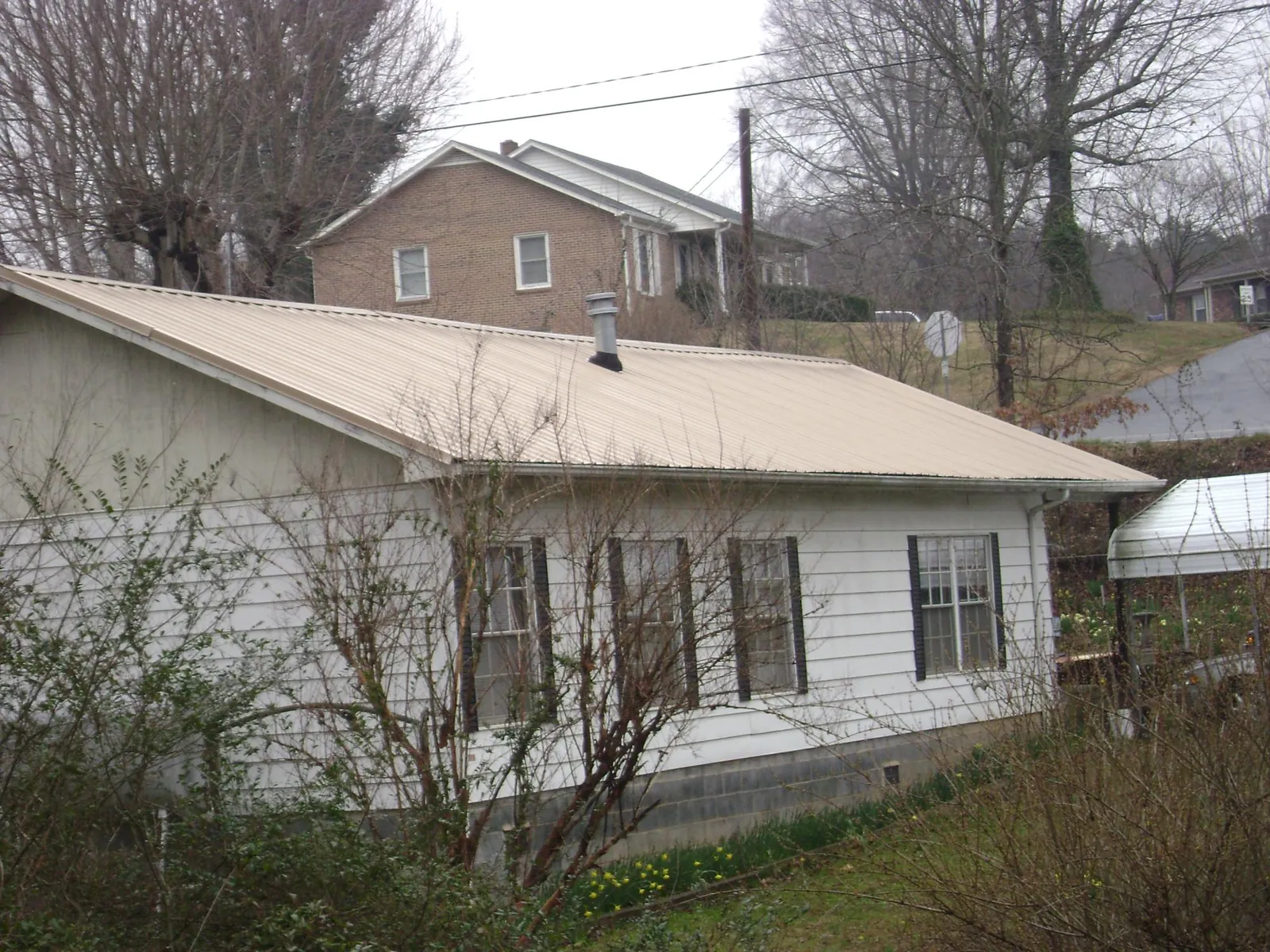 Tan metal roof on a white sided house set into a hillside — Commercial Roofing by Roofing Brothers in Granite Quarry
