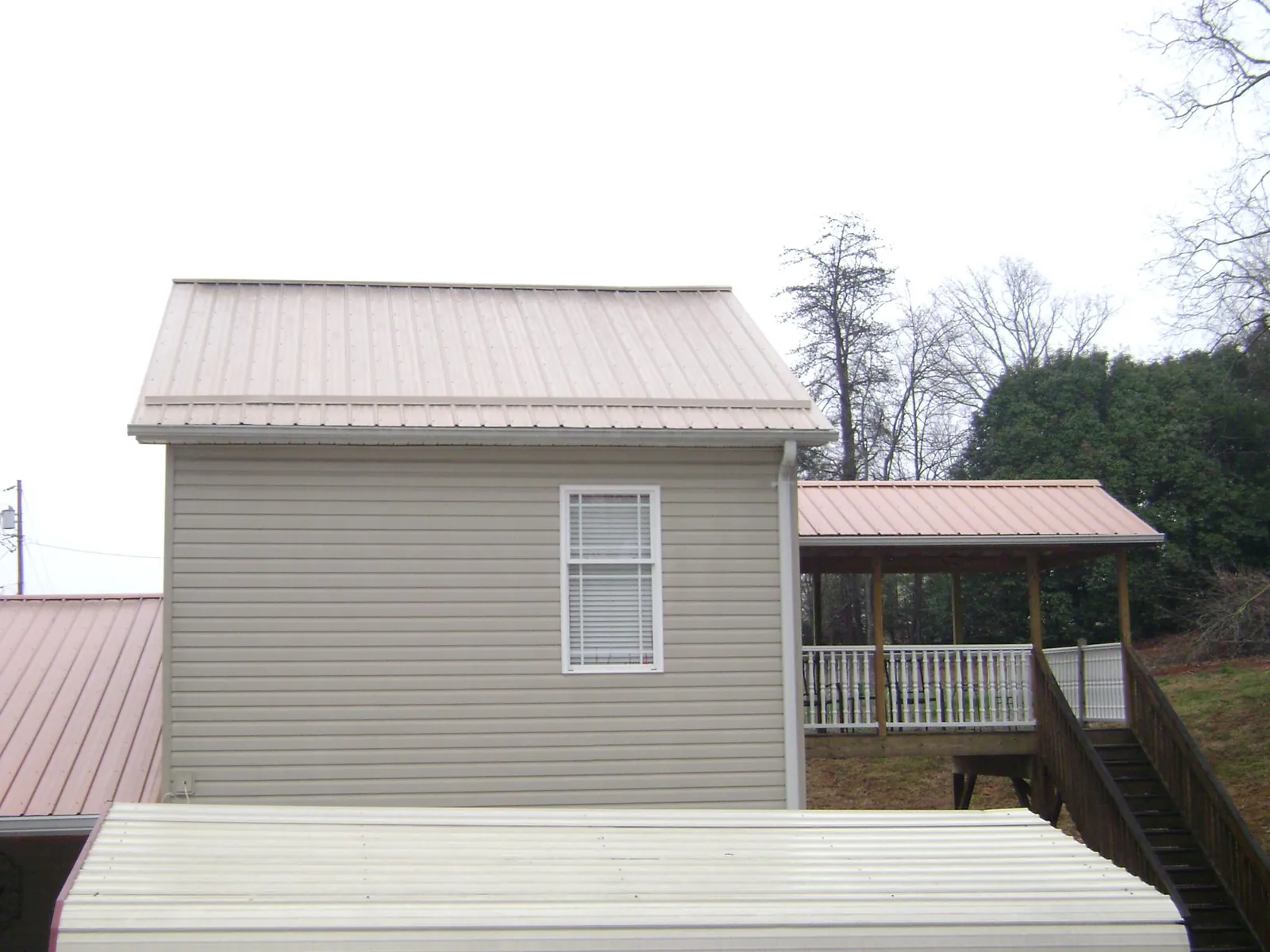 Tan metal roofs on a two story addition and attached porch, from a Roof Replacement job in Granite Quarry